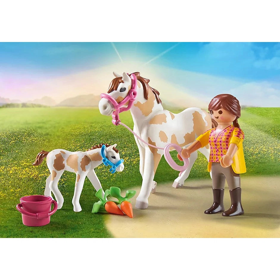 The same image from the box is shown. Both horses have bridles on and there is a pink bucket and 2 toy carrots at their feet