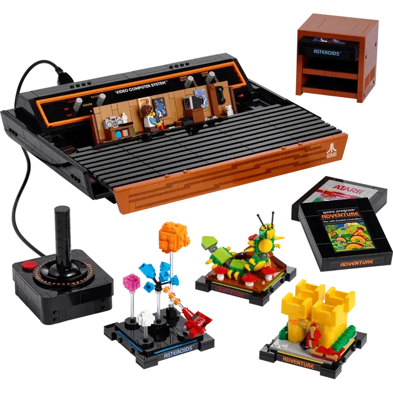 Image shows The lego atari with its base opened up to reveal a little diorama of a boy playing atari on an old school tv. There are 3 small models inspired by the three games. There is a small game storage cabinet with one of the lego cartriges in the top of the three shelves.