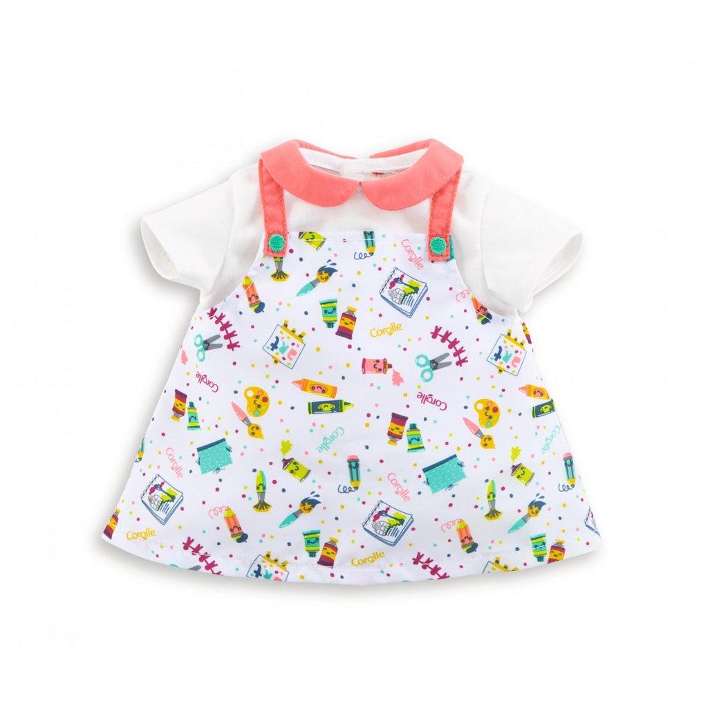 The dress consists of a pink collared white shirt under a dress styled like overalls with straps for the shoulders. The dress' pattern is an array of pencils, scissors, and other craft materials pasted all over it.