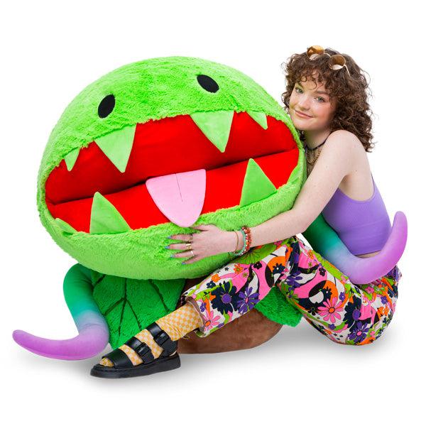 Image of the Massive Venus Fly Trap squishable. It is a humongous smiling venus fly trap plush sitting in a pot. It has a tongue sticking out and purple vines.