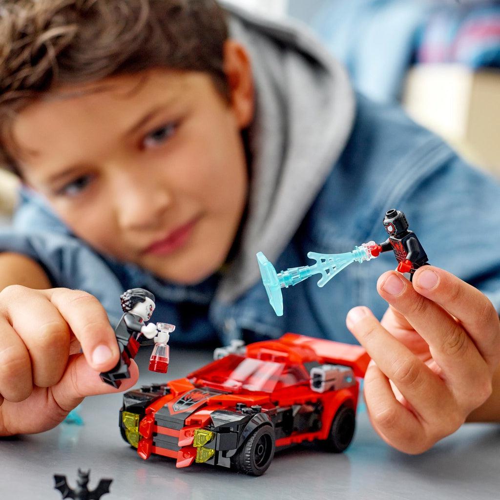 a child plays with the lego set, holding up spiderman and morbius
