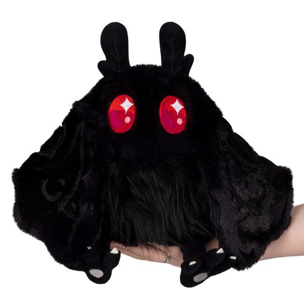 Image of the Mini Baby Mothman squishable. It is a completely black moth plush except for its amazing bright red eyes. It has large bat-like wings, clawed feet, and thin moth antennae.