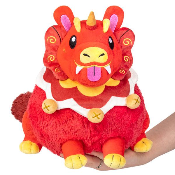 Image of the Mini Guardian Lion squishable. It is a red Chinese lion. It has many yellow accents such as bells along its collar and a yellow unicorn horn.