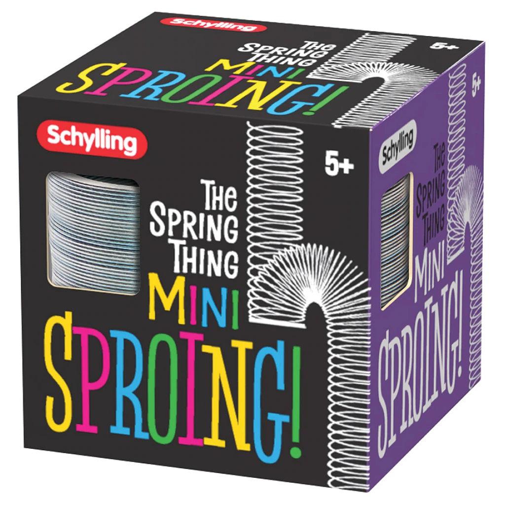 The packaging reads: The Spring Thing Mini Sproing!; The last two words are printed in various colors. The schylling logo is in the top left and 5+ is printed in the top right. There is a graphic of a spring falling down and bouncing off the word sproing as if it were a stair. There is a window cutout showing the side of the sproing inside the box. The front of the box is copied onto all 6 faces of the packaging as well