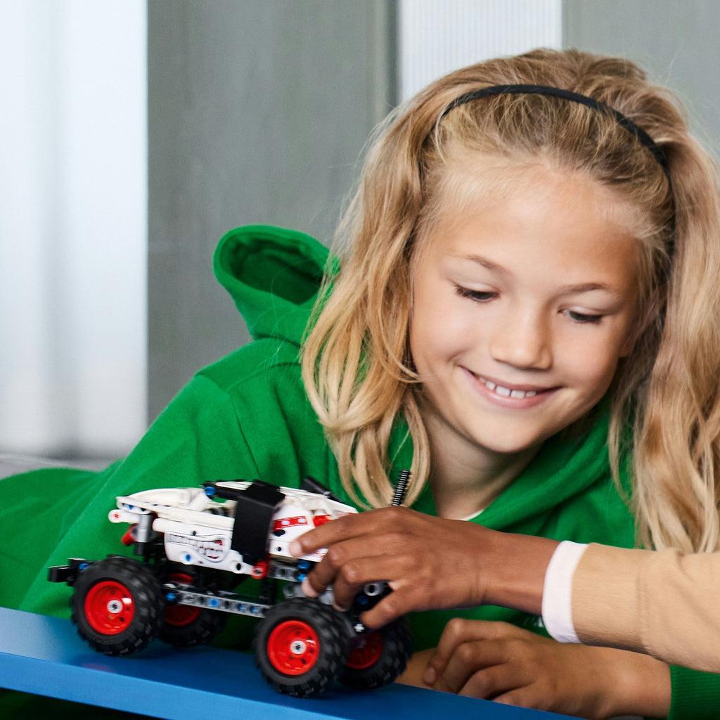two children play with the lego vehicle driving it up a ramp, only the hands of the second child who is currently holding the vehicle are visable