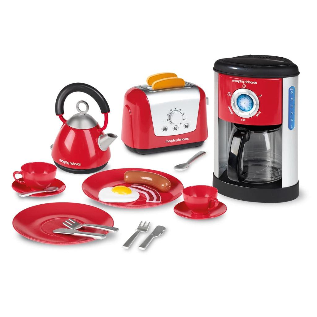 Image of all the included parts outside of the packaging. The set is bright red in color and includes a coffee maker, a kettle, a toaster, two plates, two cups and saucers, two full sets of utensils, two pieces of toast, and an egg and a sausage.