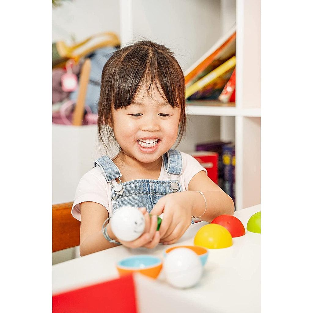 Young, smiling toddler plays with toy sitting at table.