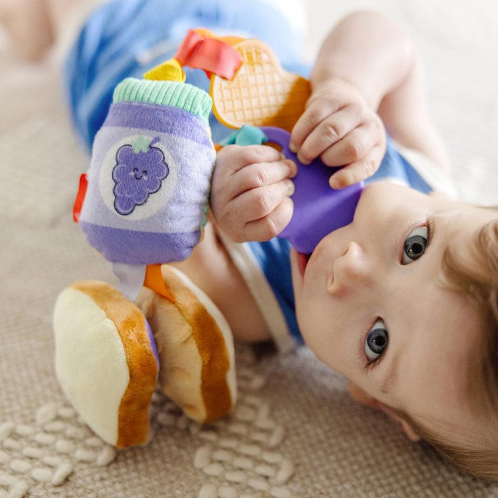 Infant lays on ground holding toy with plastic purple grape portion in mouth