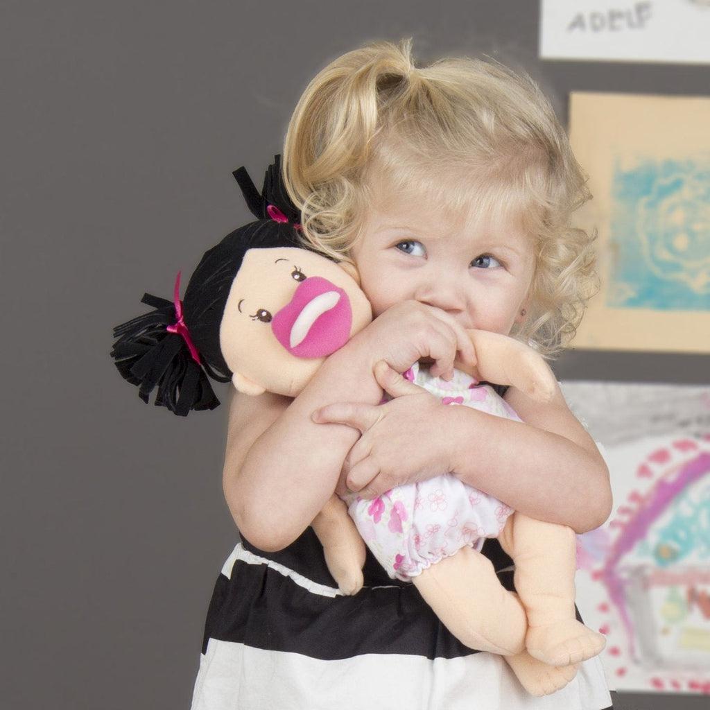 A small girl is shown hugging the doll and half hiding behind her arms and the doll.