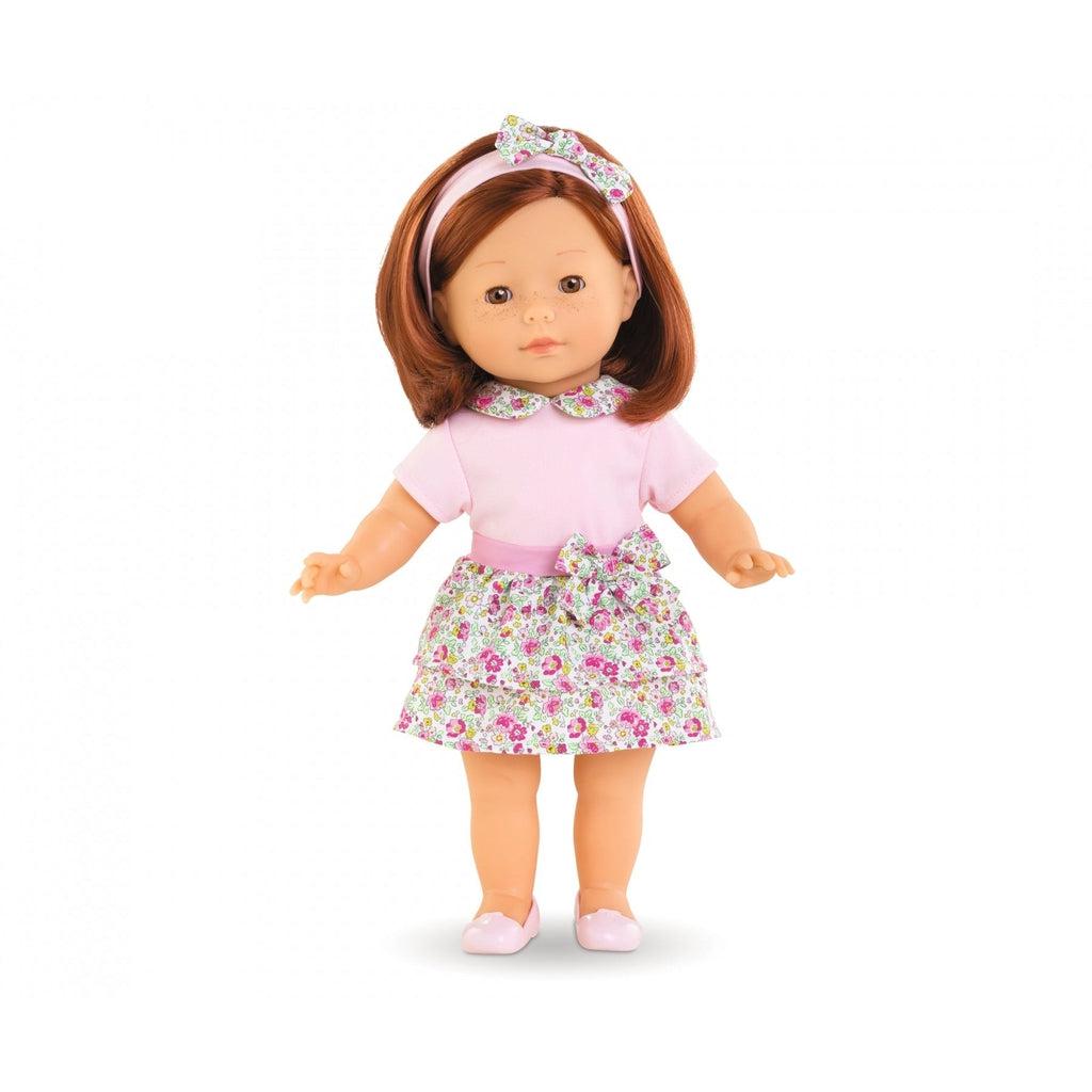 The pia doll has shoulder length ginger hair, she's wearing a pink shirt with a skirt that has red flowers and green vines printed thickly on it. The doll also has a pink headband and shoes, the headband has a bow with the same pattern as the skirt
