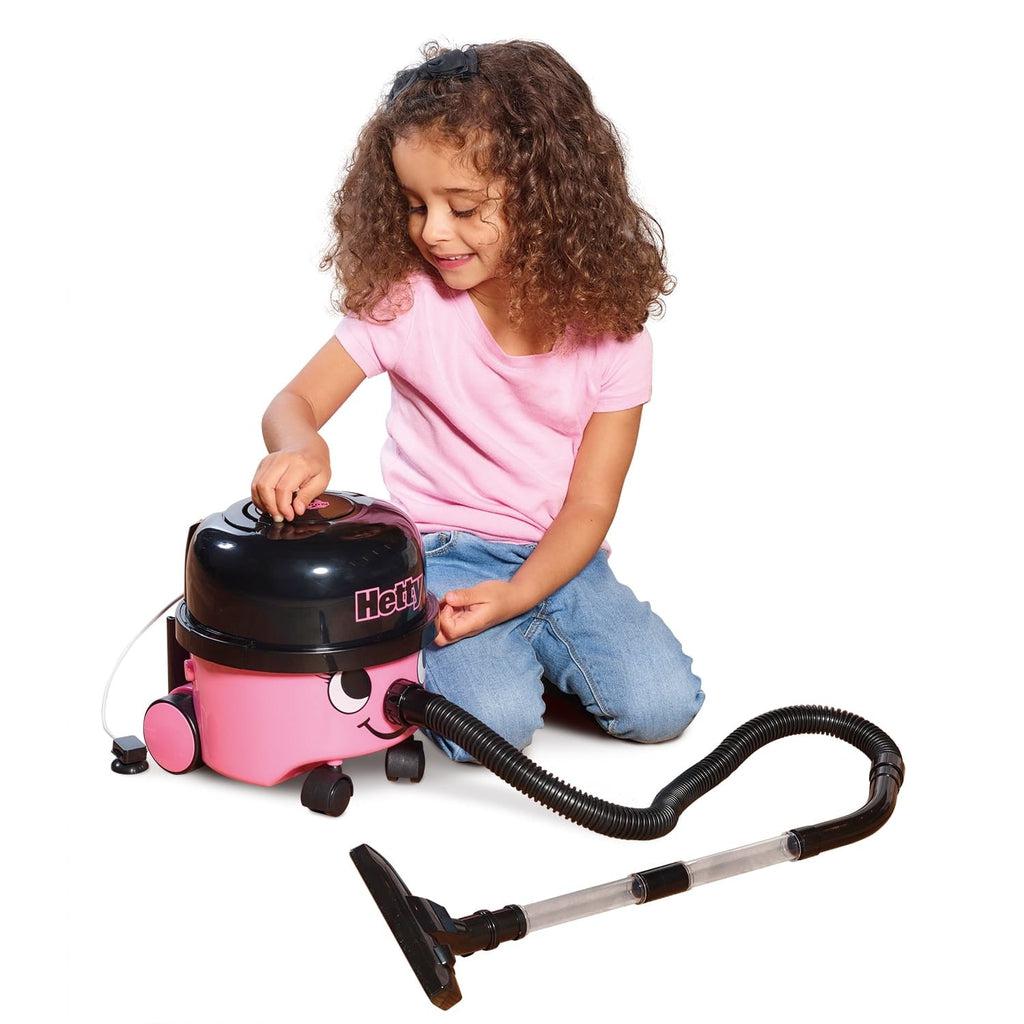 Scene of a little girl smiling and trying to open the top of the vacuum.