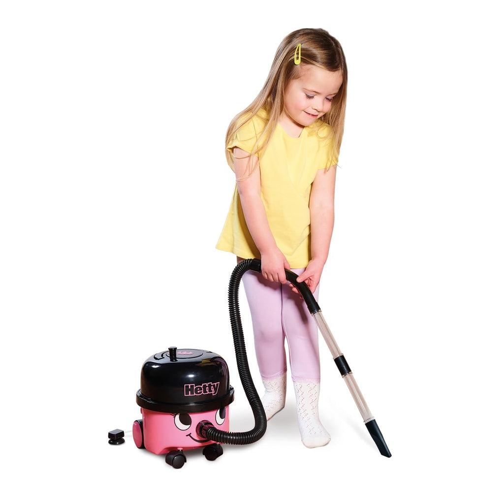 Scene of a little girl smiling and concentrating while using the vacuum to clean.