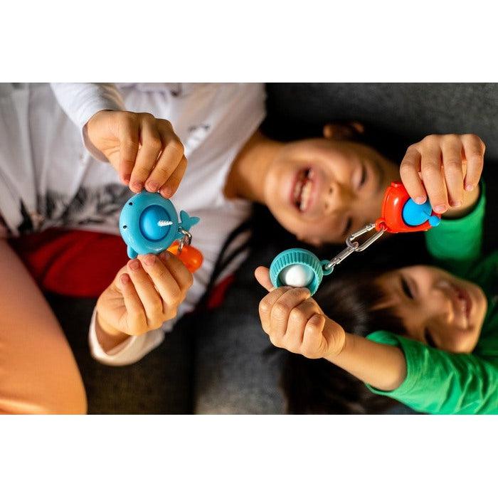 two children are seen smilling and playing with a pull n' pop each. The child on the left is holding the narwhal popper and the one on the right is holding a cupcake popper attached to a car popper by the keychain. Cupcake and Narwhal popper not included in this product, but is also available on the red balloon site.