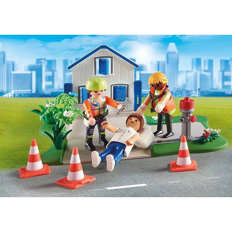 two playmobile emergency service workers treat another playmobil figure in front of the playmobile house front and next to a fire hydrant.