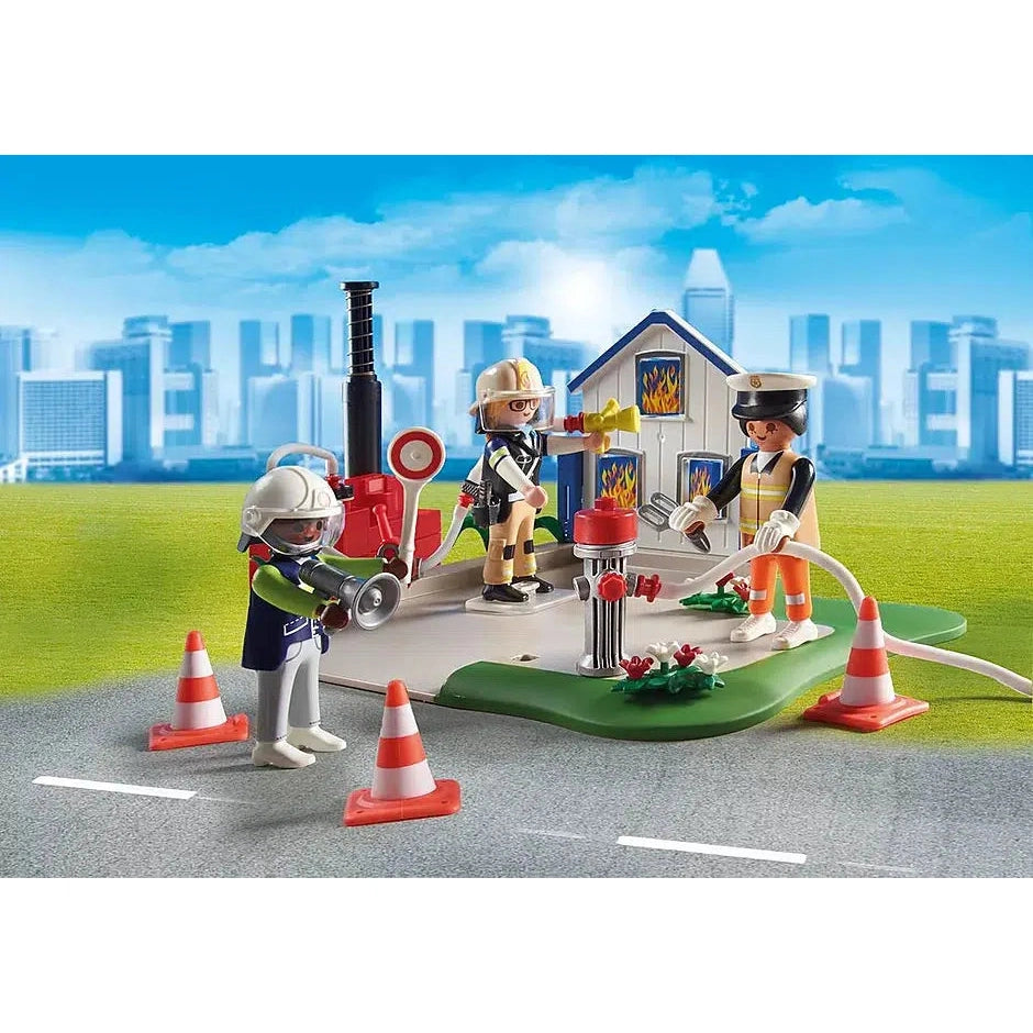 one playmobil figure attaches the hose to the fire hydrant, another prepares to spray the hose at the "burning" house, and a third stands away with a bullhorn