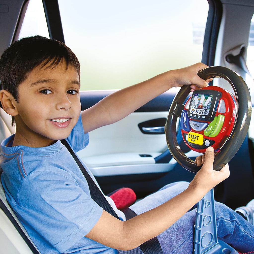 Scene of a little boy smiling while using his steering wheel in the car.