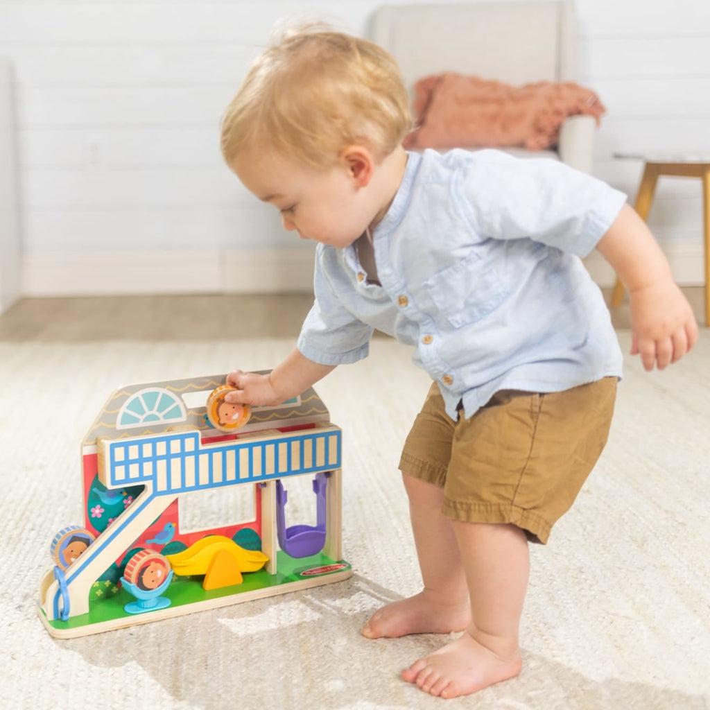 Young toddler stands playing with toy, ready to drop wooden disk down 3D slide portion of toy