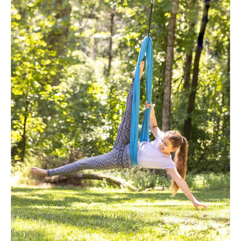 A young girl does a pose in the swing, stretching out horizontally and lifting one of her legs into the air and wrapping her foot around the top of the swing for support.