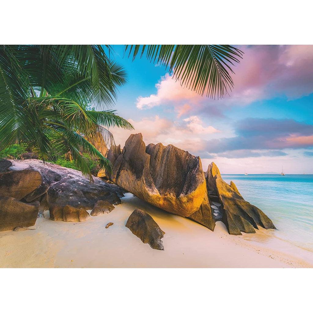 Puzzle image | Tranquil beach scene | Palm trees sit behind the beach and rocky protrusions cover most of the beaches soft sand | Turquoise water meets the beach and a colorful sunrise sky.