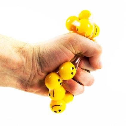 A man is squeezing the stress ball, pushing the smiley face balls inside to either end as they bulge outwards.