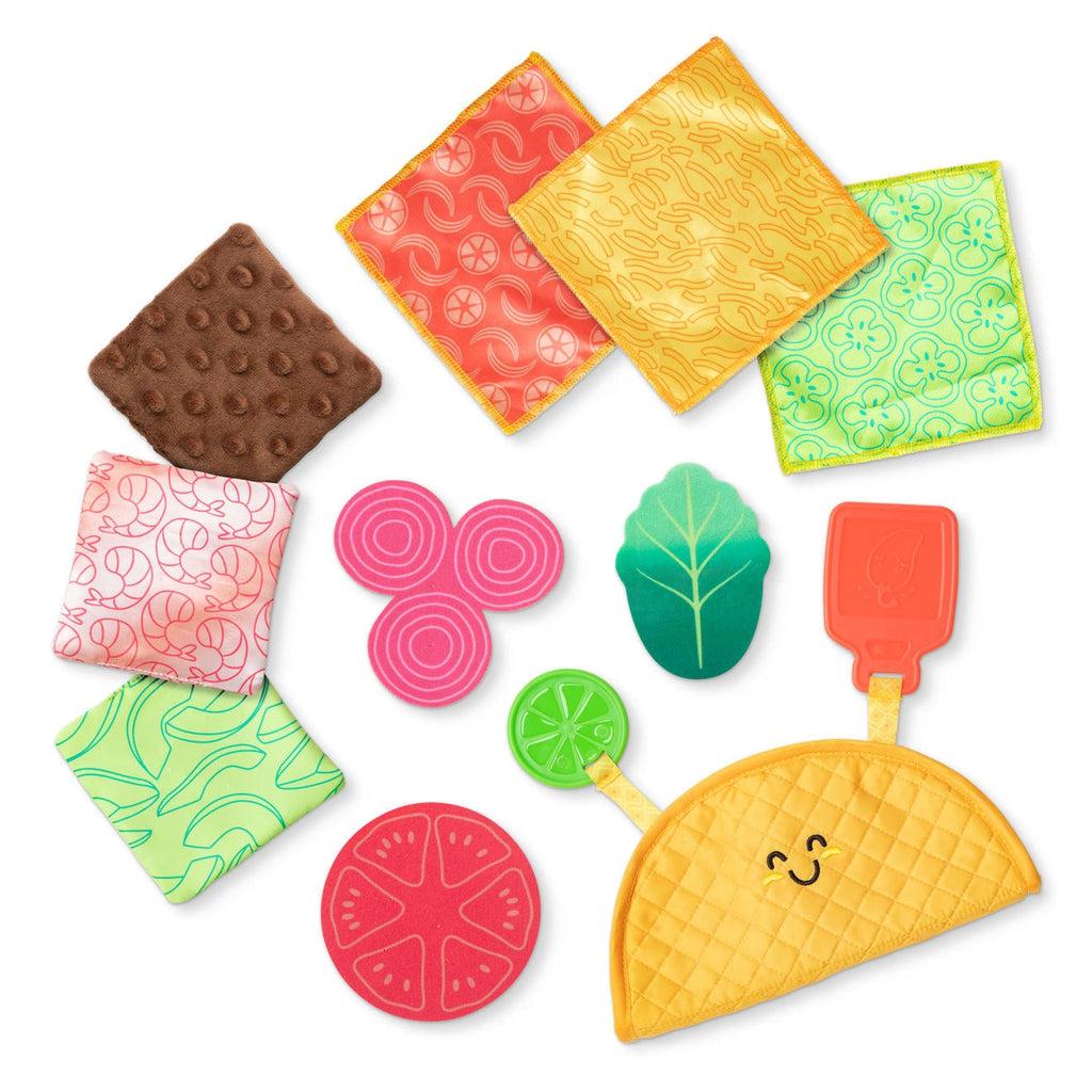 Toy out of package | Foam taco shell with attached plastic lime and hot sauce packet | 3 textured, crinkle fabric food pieces | 3 smooth fabric pieces | 3 food-shaped fabric pieces