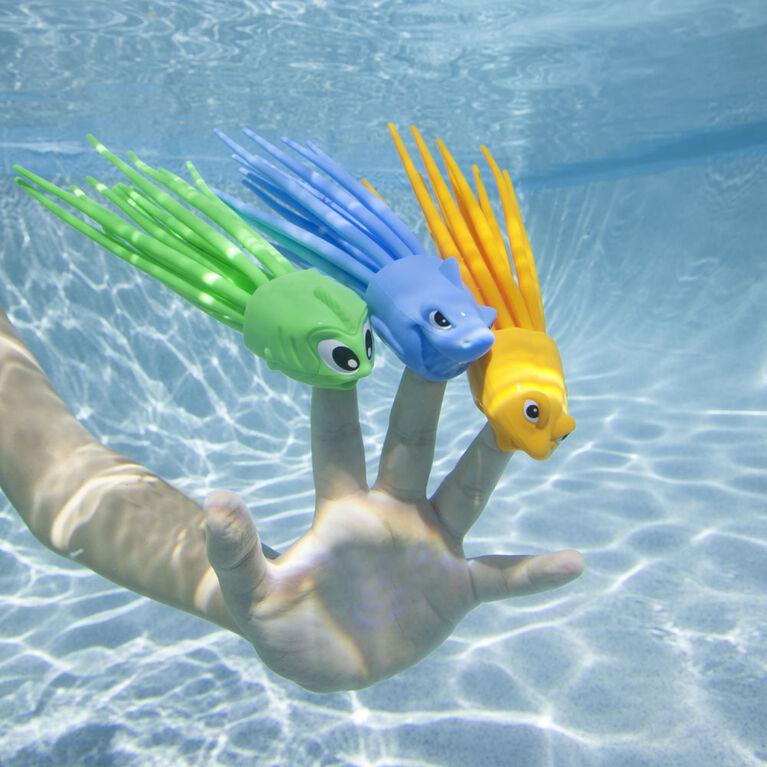 the three dive toys are shown on the fingers of a kids hand. One has a shark face, one has a fish face, and the third has a elongated fish face. Each has a handful of rubber tentacles trailing out the back.
