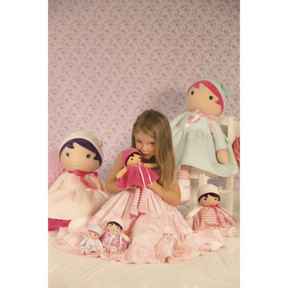 A girl is shown sitting down surrounded by the same doll but in various sizes ranging from smaller than her head to one nearly as big as her.