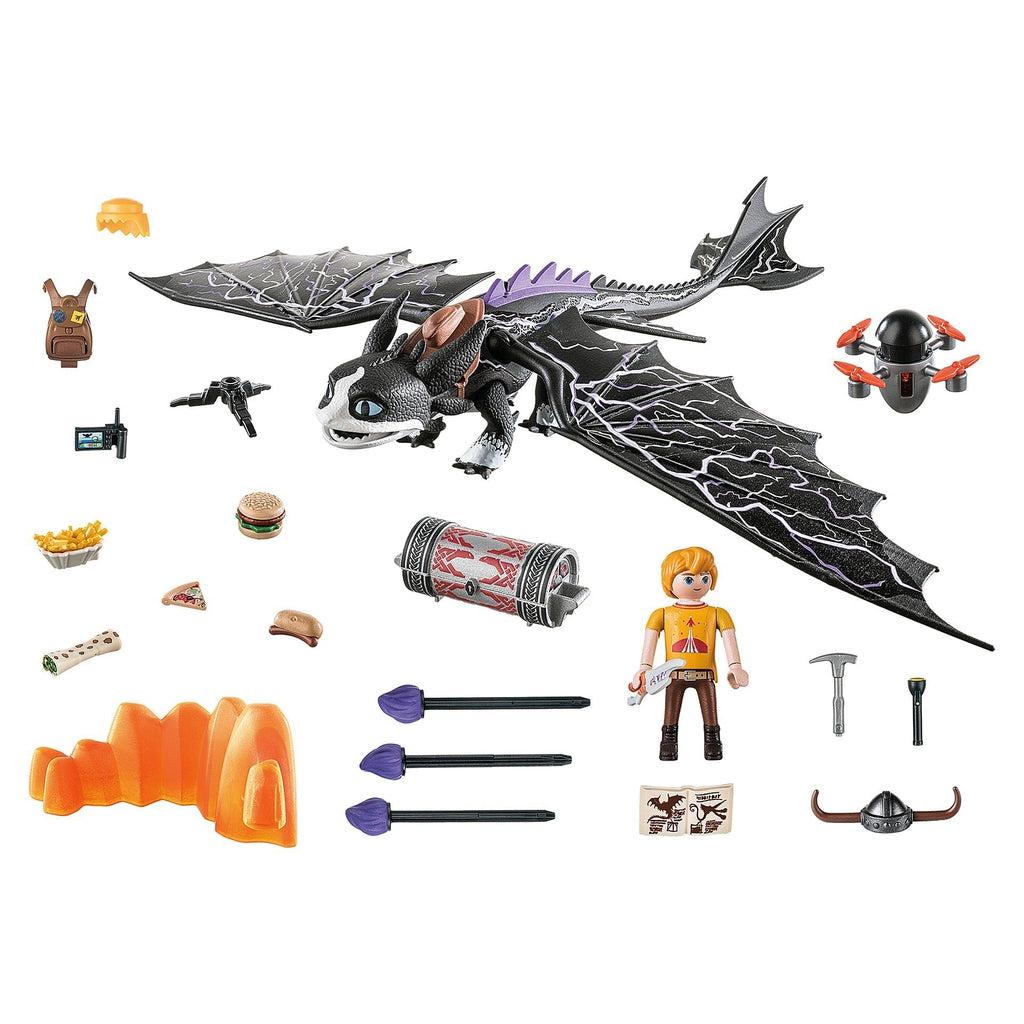 Image of all the included pieces in the set outside of the packaging. It includes a large black and white dragon, Tom the dragon rider, a drone, and various supplies and food items.