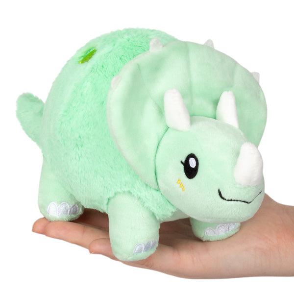 Image of the Triceratops Snacker plush. It is a light mint green with white horns. It is smiling and it has a generally round shape to it.
