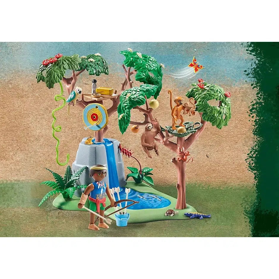 The other half of the playset is shown. There's a rock with waterfall decals on it. A tree on top of the rock has an archery target on it and a parrot perched near a wooden platform in the branches, another tree at the base of the rock has 3 monkey figures on it and a sloth