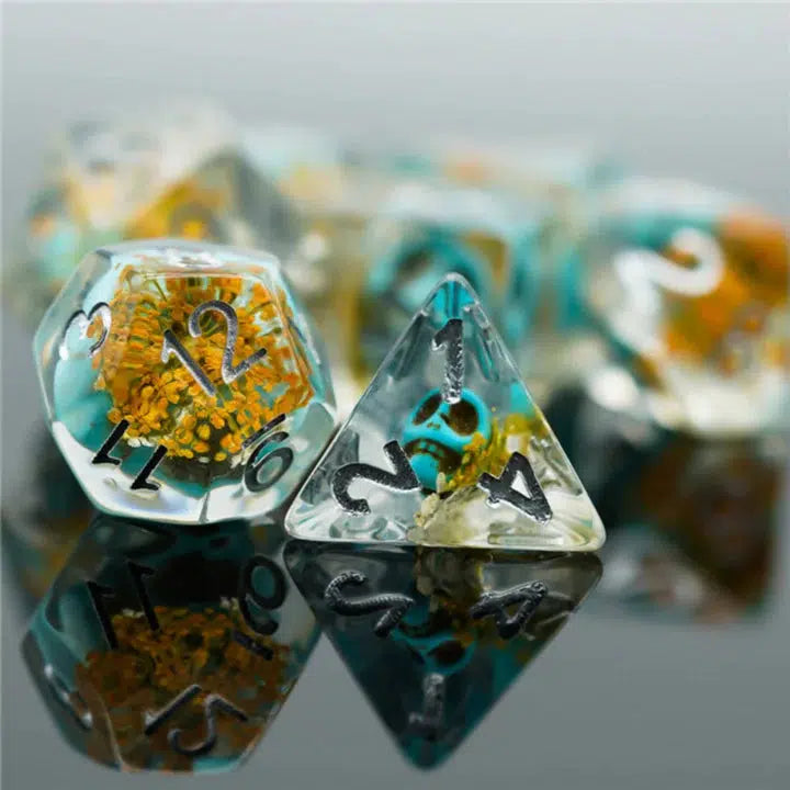 The D12 and D4 are shown with the rest out of focus in the back. They are clear resin with a blooming yellow flower and a small blue skull inside each.